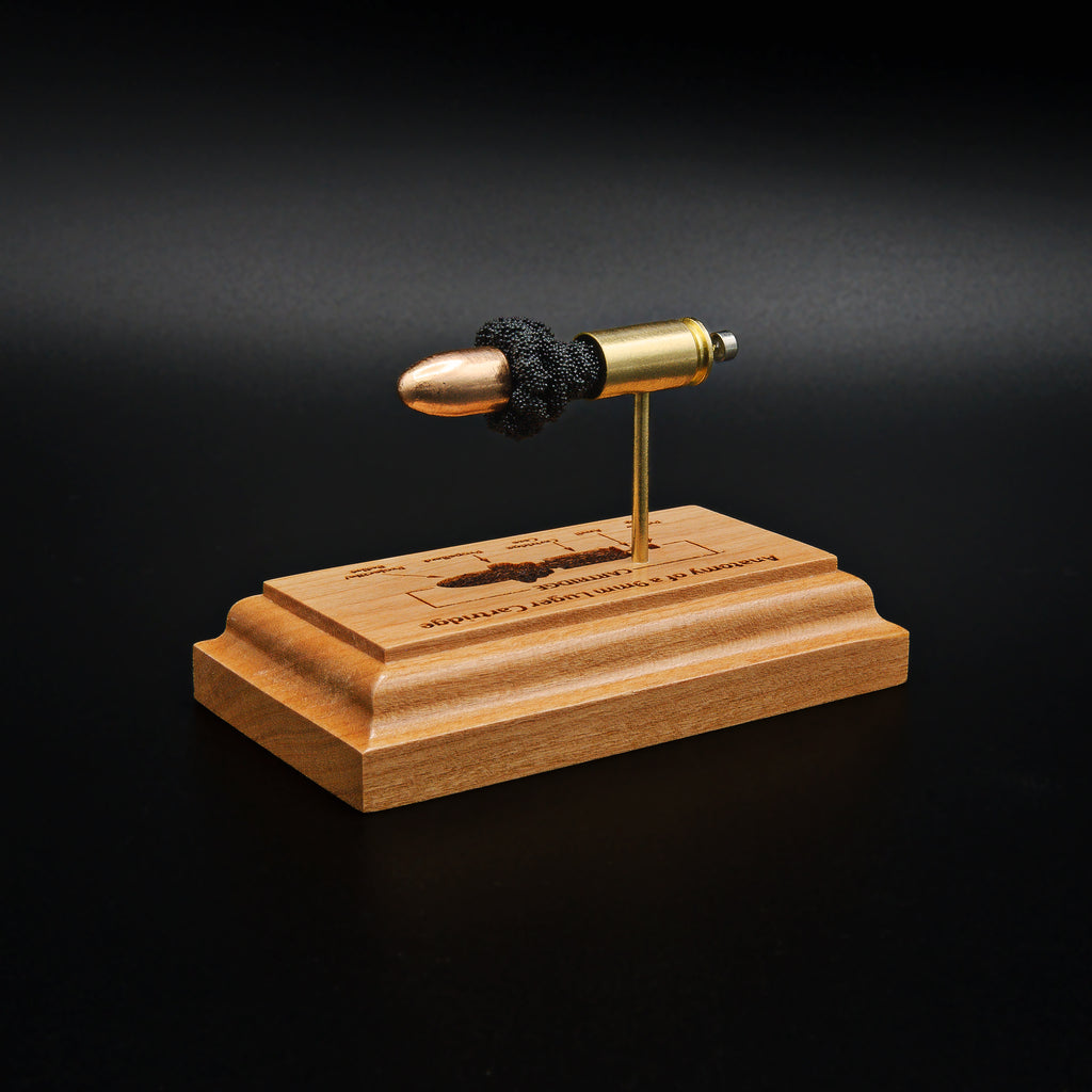 Left back angled view of a handcrafted 9mm Luger cartridge anatomy display featuring a 115gr Sierra FMJ bullet with an engraved anatomy diagram showing the primer cup, anvil, cartridge case, powder, and projectile that is mounted on a solid cherry wood base.