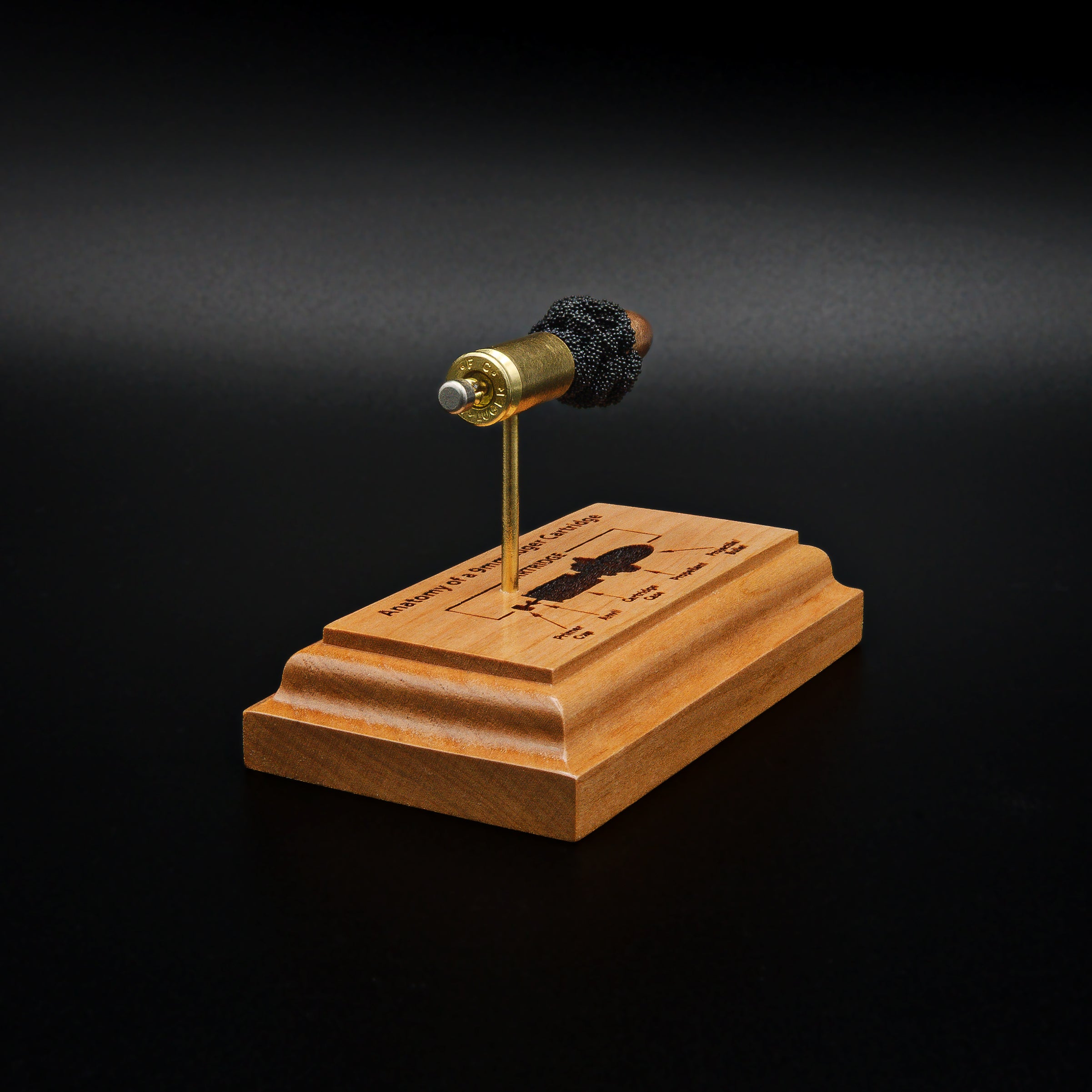 Rear view of a handcrafted 9mm Luger cartridge anatomy display featuring a 115gr Sierra FMJ bullet with an engraved anatomy diagram showing the primer cup, anvil, cartridge case, powder, and projectile that is mounted on a solid cherry wood base.