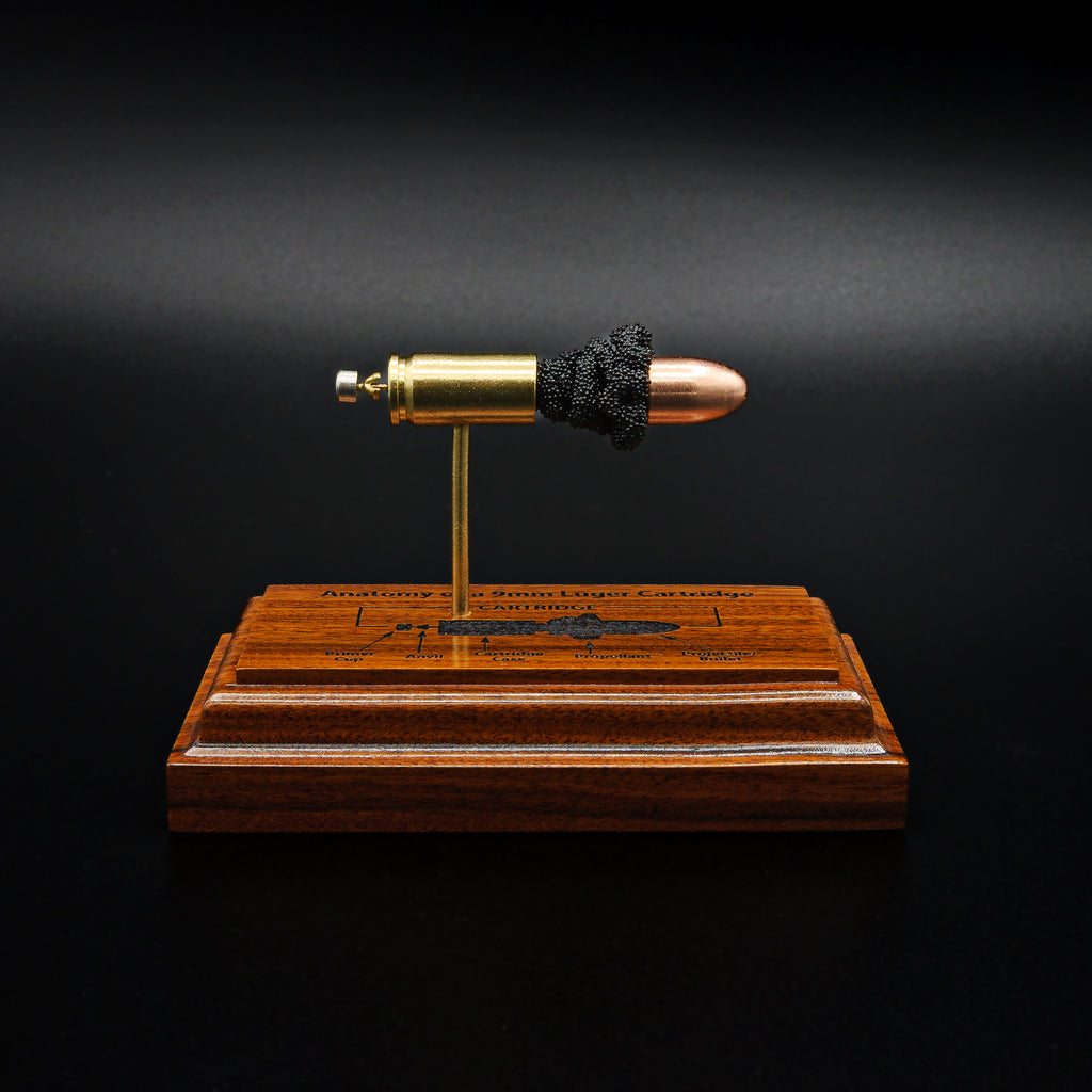 Front view of a handcrafted 9mm Luger cartridge anatomy display featuring a 115gr Sierra FMJ bullet with an engraved anatomy diagram showing the primer cup, anvil, cartridge case, powder, and projectile that is mounted on a solid bolivian rosewood base.