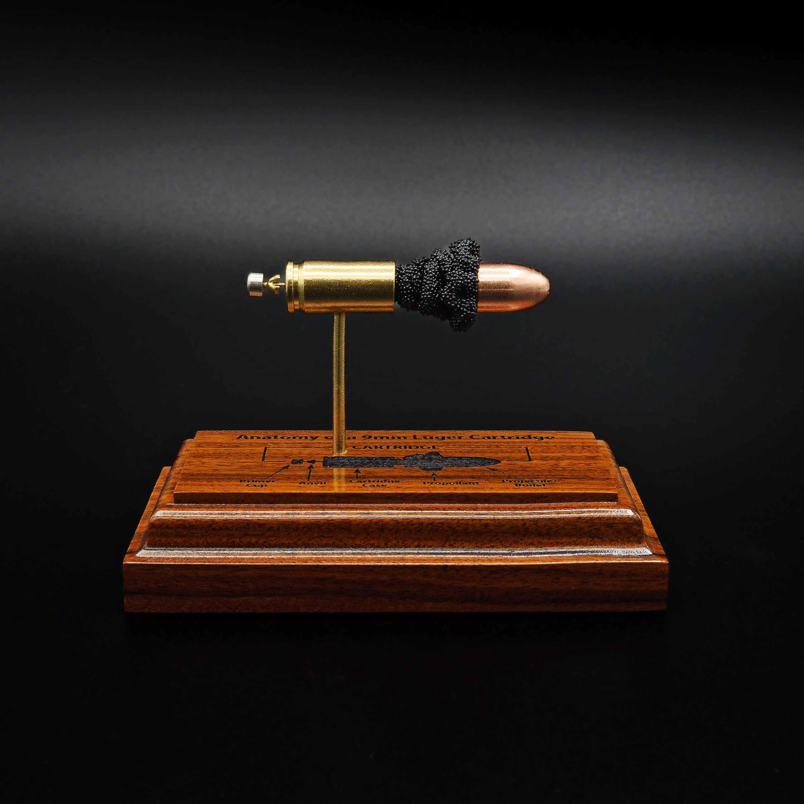 Front view of a handcrafted 9mm Luger cartridge anatomy display featuring a 115gr Sierra FMJ bullet with an engraved anatomy diagram showing the primer cup, anvil, cartridge case, powder, and projectile that is mounted on a solid bolivian rosewood base.
