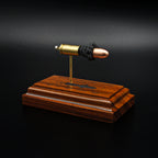 Front angled view of a handcrafted 9mm Luger cartridge anatomy display featuring a 115gr Sierra FMJ bullet with an engraved anatomy diagram showing the primer cup, anvil, cartridge case, powder, and projectile that is mounted on a solid bolivian rosewood base.