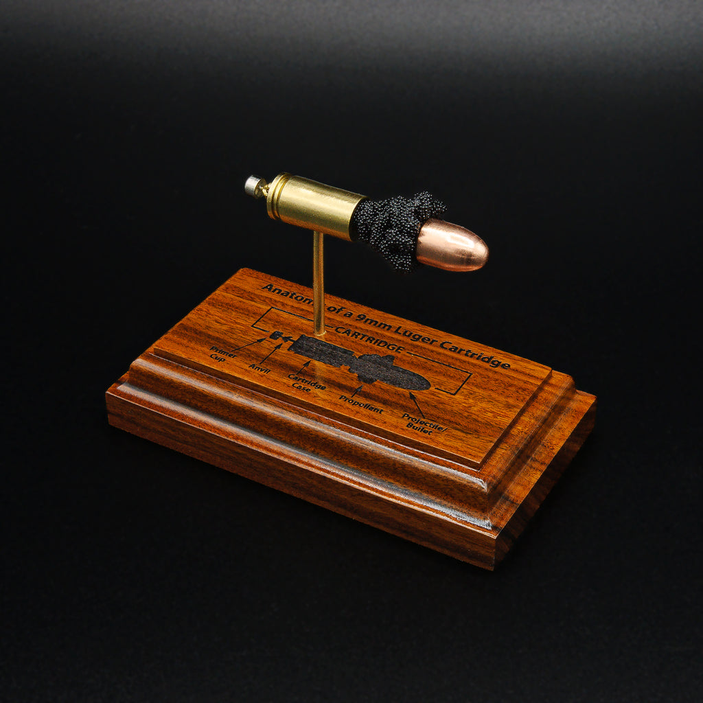 Elevated front right angled view of a handcrafted 9mm Luger cartridge anatomy display featuring a 115gr Sierra FMJ bullet with an engraved anatomy diagram showing the primer cup, anvil, cartridge case, powder, and projectile that is mounted on a solid Bolivian rosewood base.