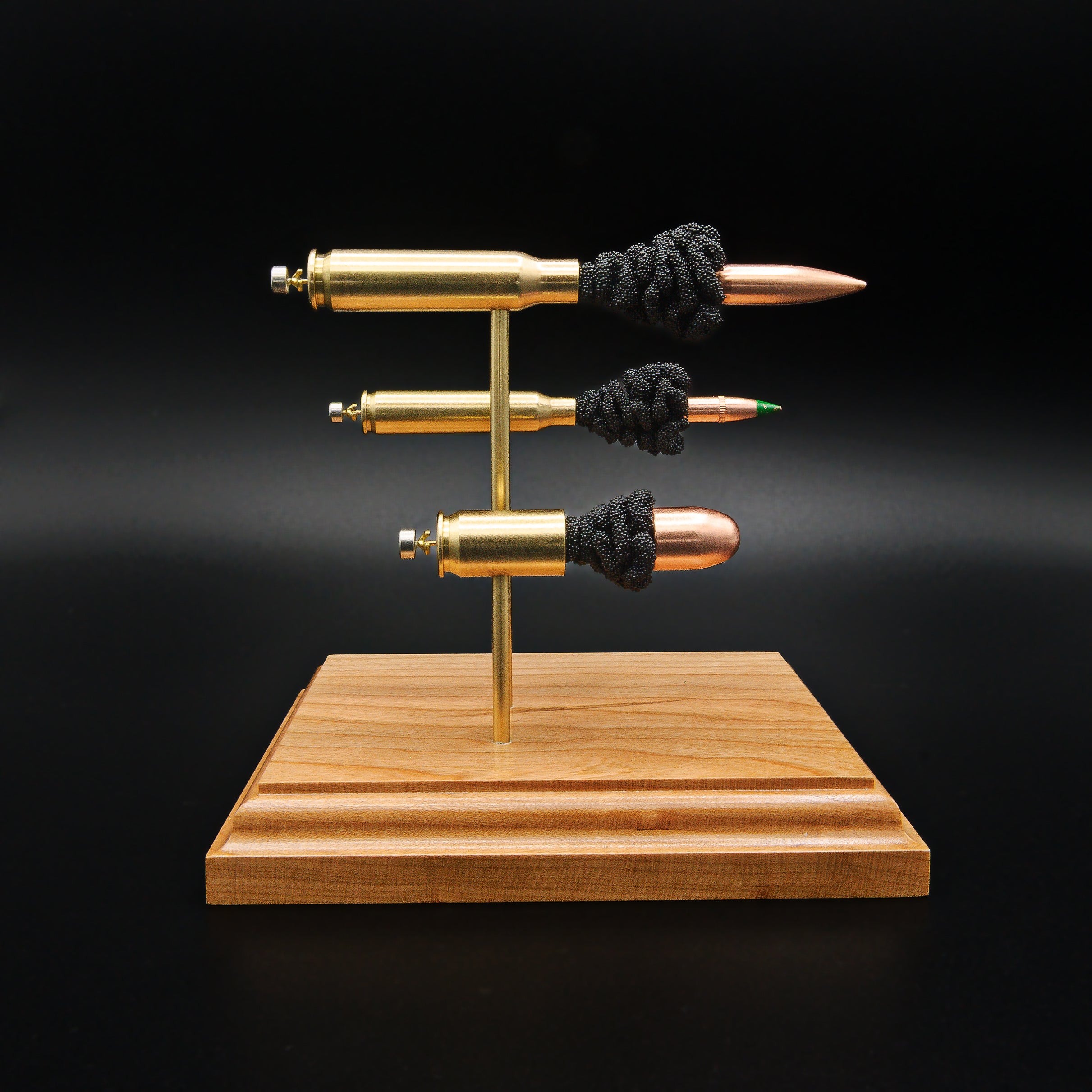 Side view of a handcrafted triple caliber exploded ammunition display featuring a .308 Winchester 168gr Sierra MatchKing HPBT, 5.56×45mm M855 Green Tip, and .45 Auto 220gr Sierra FMJ mounted on a premium cherry wood base.