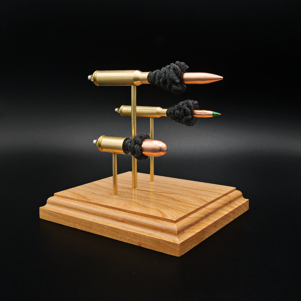 Front left angle of a triple caliber anatomy ammunition display showcasing a .308 Winchester Sierra MatchKing HPBT, 5.56×45mm M855 Green Tip, and .45 Auto Sierra FMJ with simulated powder on a handcrafted cherry wood base.