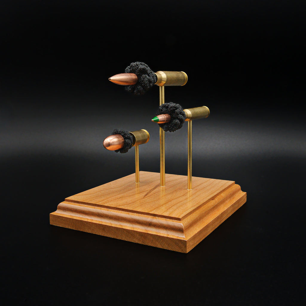 Front right perspective of a handcrafted triple caliber ammunition display featuring a .308 Winchester 168gr Sierra MatchKing HPBT, 5.56×45mm M855 Green Tip, and .45 Auto 220gr Sierra FMJ mounted on a cherry wood base.