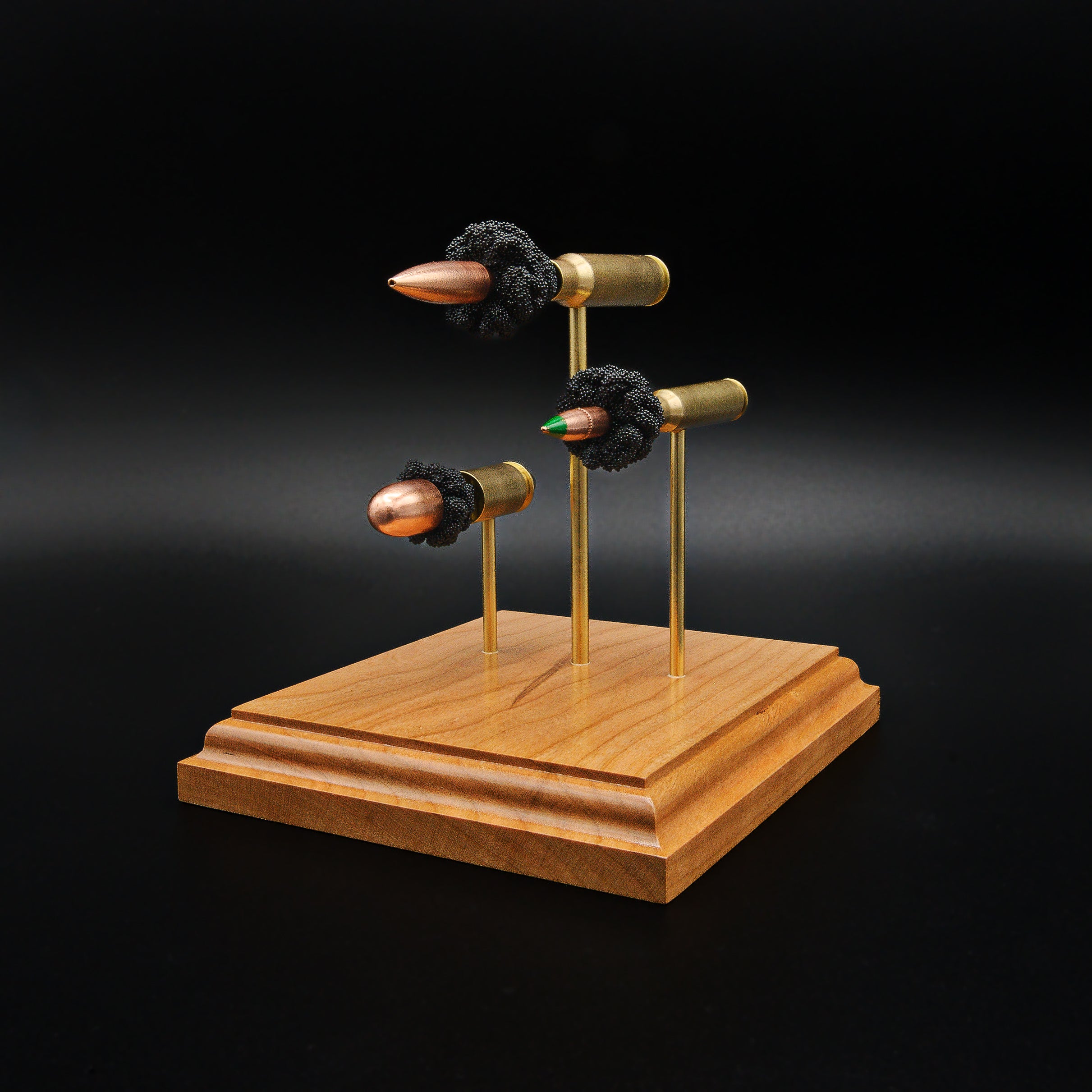 Front right perspective of a handcrafted triple caliber ammunition display featuring a .308 Winchester 168gr Sierra MatchKing HPBT, 5.56×45mm M855 Green Tip, and .45 Auto 220gr Sierra FMJ mounted on a cherry wood base.