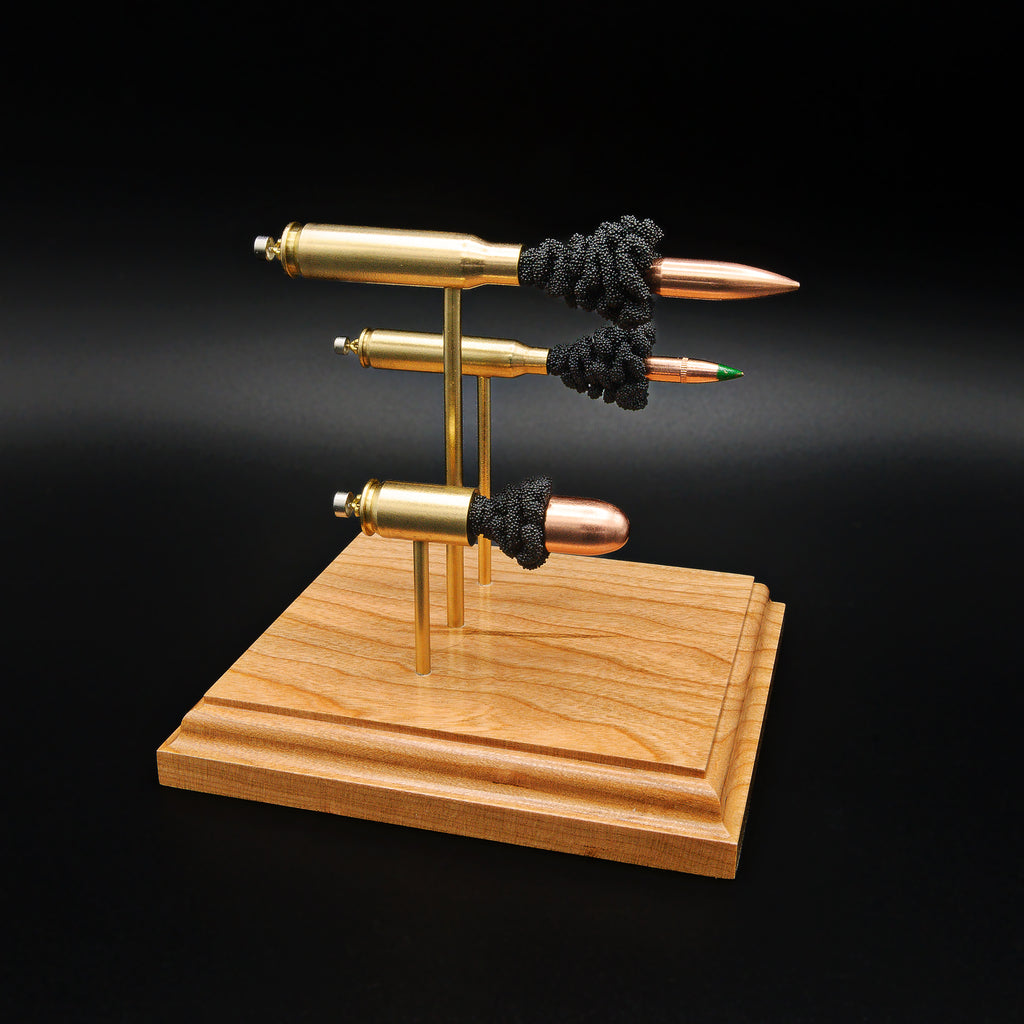 Angled front view of a triple caliber exploded ammunition display showcasing a .308 Winchester 168gr Sierra MatchKing HPBT, 5.56×45mm M855 Green Tip, and .45 Auto 220gr Sierra FMJ with simulated powder on a handcrafted cherry wood base.